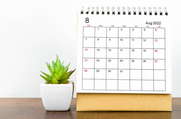 The August 2022 desk calendar with plant on wooden table.