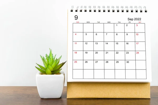 The September 2022 desk calendar with plant on wooden table.