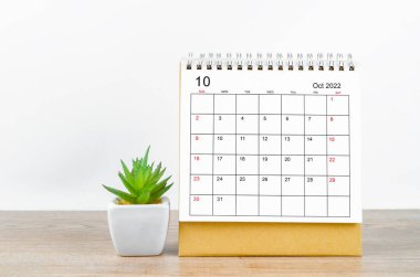 October 2022 desk calendar with plant on wooden table.