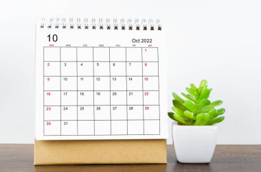 October 2022 desk calendar with plant on wooden table.