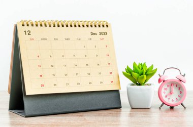 December 2022 green Desk calendar with pink alarm clock on wooden table.