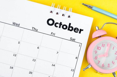 October 2022 desk calendar and pen with plant pot on yellow background.