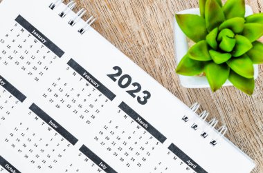 12 months desk calendar 2023 with pen on wooden background.