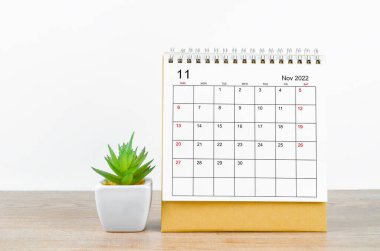 November 2022 desk calendar with plant on wooden table.
