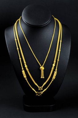 Necklace display stand with gold necklace on black background.