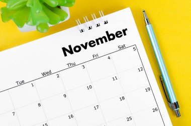 November 2022 desk calendar and pen with plant pot on yellow background.