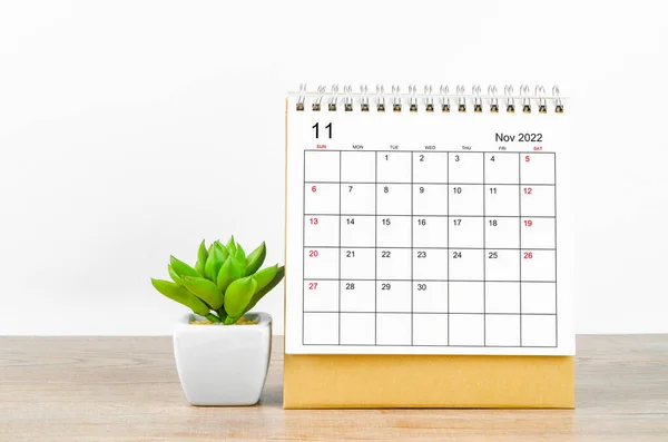 November 2022 desk calendar with plant on wooden table.