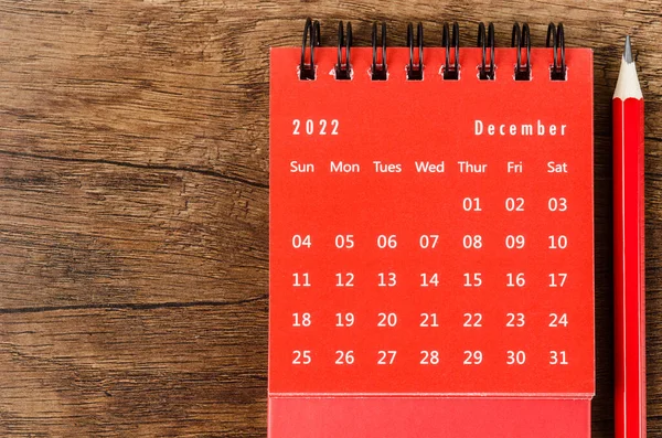 Red December 2022 Monthly desk calendar for 2022 year with red pencil on wooden background.