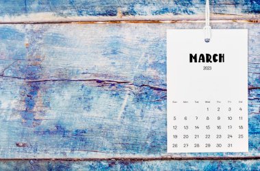 Mart 2023 takvim sayfası eski mavi ahşap arka planda beyaz iple asıldı.