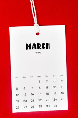 Mart 2023 takvim sayfası Kırmızı arkaplanda beyaz ipe asıldı.