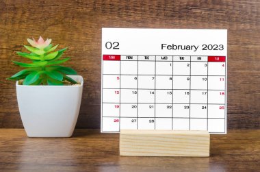 2023 Şubat ayının takvimi. Ahşap masa üzerinde saksı var..