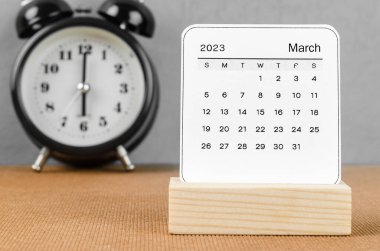 2023 Mart ayının takvimi. Ahşap masa üzerinde çalar saat..