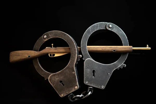 A wooden rifle in metal handcuffs on an isolate of black color. The law on weapons. Arrest. — Stock Photo, Image