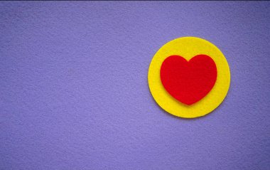 Sarı dairede kırmızı tekstil kalp ve mor arka plan. Keçeli kumaştan bir kartpostal. Mor arka planda romantik metin için bir yer.