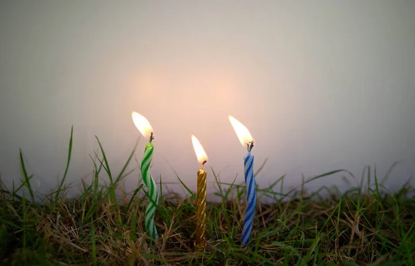Três velas estão presas no chão contra um fundo de isolamento branco. Velas na grama verde. — Fotografia de Stock