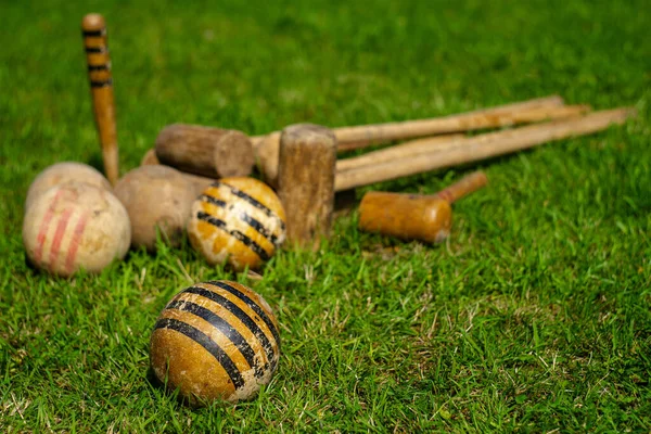 Bahçedeki yeşil çimlerin üzerinde klasik kroket seti. Çimenlerde oynamak için topları olan tahta sopalar..