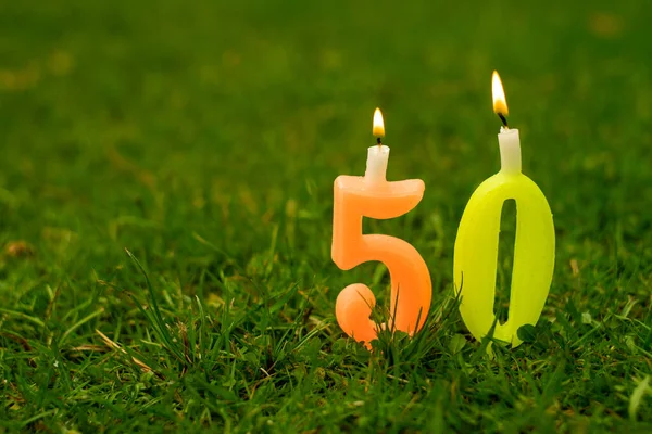 Festive candles in the form of numbers 50 in the green grass. festive background for the text for the anniversary. — Stockfoto