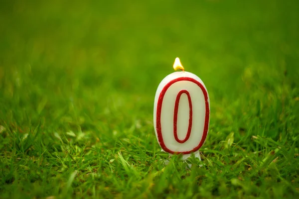 Hořící svíčka s číslem nula na zelené trávě. — Stock fotografie