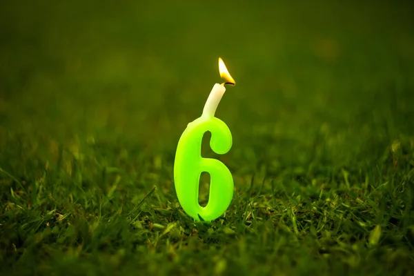 Uma vela acesa na forma do número 6 na grama verde — Fotografia de Stock