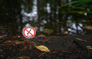 A red sign forbidding jumping into a pond. It is forbidden to jump into the water.