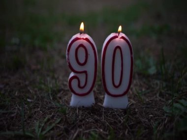 A burning candle with the number 90. Congratulatory background for the 90th anniversary. A candle flame with a number on the green grass.