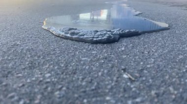 A black puddle of water spreads across the asphalt directly into the camera