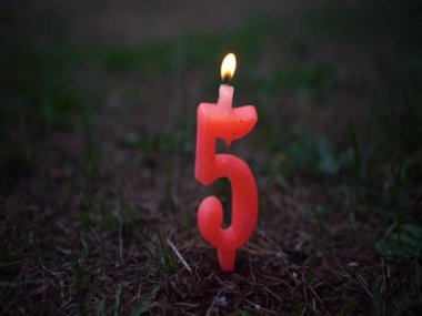 A candle in the form of the number 5 with a burning flame is stuck in the ground. Birthday greeting background. Fifth anniversary.