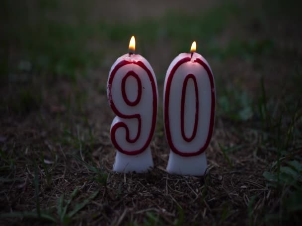 Una vela encendida con el número 90. Antecedentes de felicitación por el 90 aniversario. Una llama de vela con un número en la hierba verde. — Vídeos de Stock