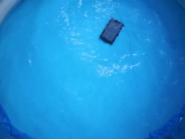 Uma mão de homem abaixa um tablet eletrônico preto na água da piscina para verificar a permeabilidade à água — Vídeo de Stock