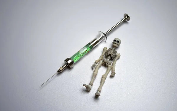 A skeleton next to a syringe on a white isolate. Death by injection. A dangerous vaccine.A glass syringe with poison. — Fotografia de Stock