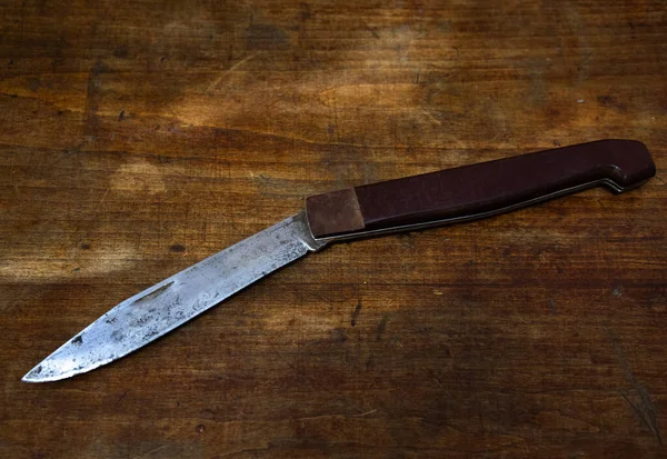 Un gran cuchillo plegable sobre una mesa de madera. Enfrentamientos penales por motivos domésticos. —  Fotos de Stock