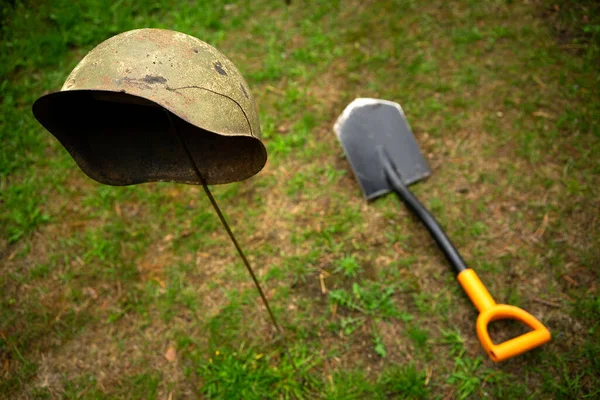 En ojordad soldathjälm och en metallspade ligger på marken.Sök efter militära artefakter. Okänd soldat. — Stockfoto