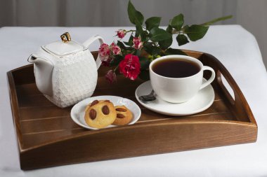 Kurabiyeli bir fincan çay ve tepside bir gül.