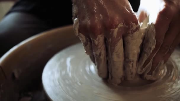 Handen van een jonge mannelijke pottenbakker die aan een pottenbakkerswiel werkt en een pot maakt — Stockvideo