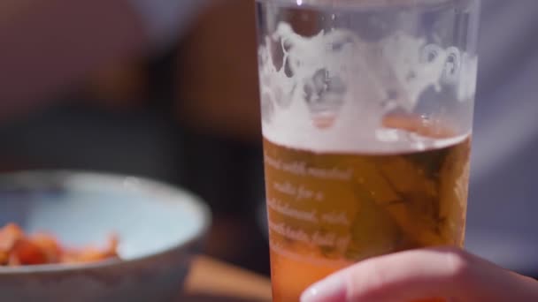 Mão segura um copo meio vazio de cerveja sentado na varanda ao ar livre de um bar — Vídeo de Stock