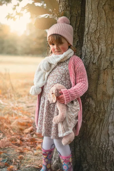 Cute little girl standing near a tree with a teddy bear — Stock Photo, Image
