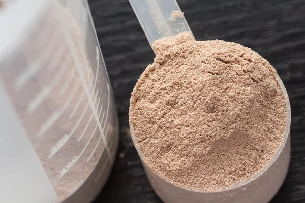 Scoop of chocolate whey isolate protein in front of protein shaker and its parts — Stock Photo, Image