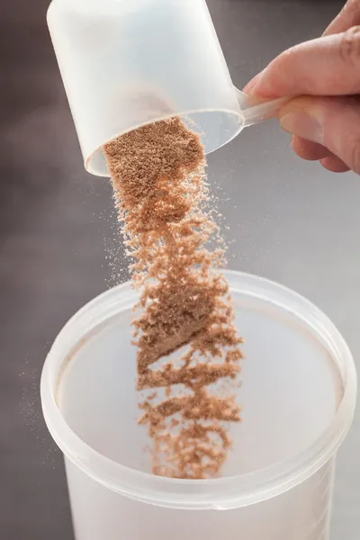 Scoop of chocolate whey isolate protein tossed into plastic white shaker, with focus on the protein in the scoop and falling protein blurred — Stock Photo, Image