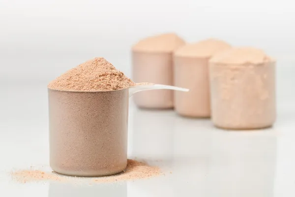 Scoop of chocolate whey isolate protein in front of three scoops of protein blurred in the background — Stock Photo, Image