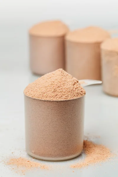 Cucharada de proteína aislada de suero de chocolate delante de tres cucharadas —  Fotos de Stock