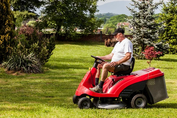 Hombre mayor conduciendo una cortadora de césped roja — Foto de Stock