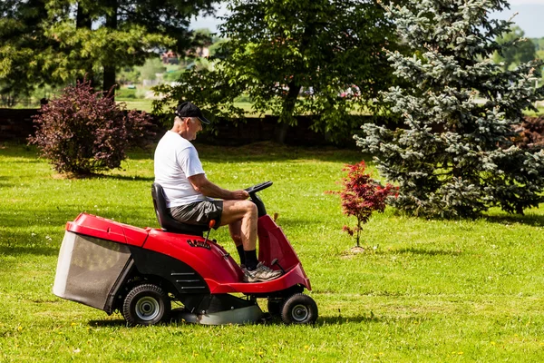 Hombre mayor conduciendo una cortadora de césped roja — Foto de Stock