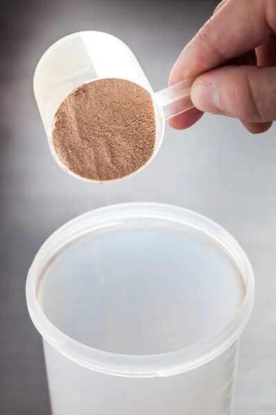 Colher de proteína isolada de soro de chocolate jogado em plástico agitador branco, com foco na proteína na colher e queda de proteína turva — Fotografia de Stock