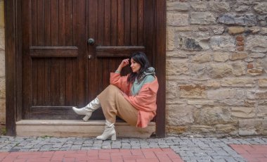 Esmer kadın ahşap kapının önünde oturuyor ve şöyle düşünüyor: