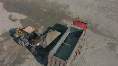 Tekerlek ön yükleyicisi taş ocağındaki, havadaki hurda kamyonuna ezilmiş taş yüklüyor.