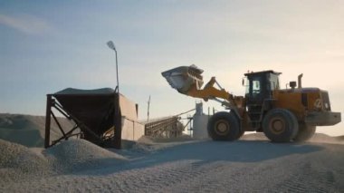 Tekerlek yükleyicisi ezicide taş yüklüyor, inşaat malzemeleri üretiminde çalışıyor