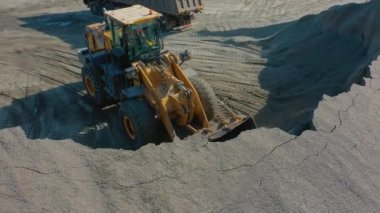 Tekerlek yükleyicisi kum yığınından kovayla moloz topluyor.
