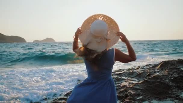 穿着夏装戴帽子的女士站在海滨，夕阳西下被海浪冲刷 — 图库视频影像