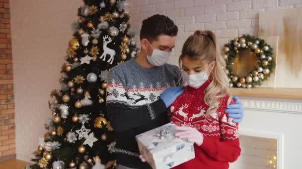 Чоловік обіймає свою дівчину, дарує подарунок на Різдво в медичних масках і рукавичках — стокове відео