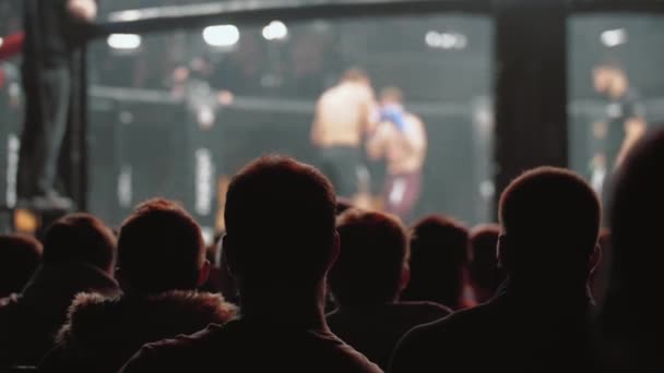 MMA-strijders sparren in bokskooi, wazig zicht achter kijkers — Stockvideo
